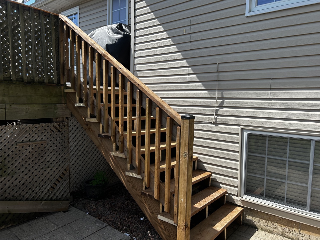 Newly rebuilt wood deck stairs with railing beside the house